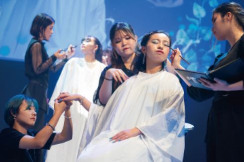 トータルビューティー科の学生がステージ上でモデルにメイクをしている様子