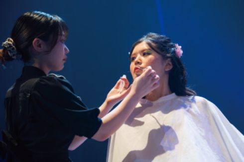 トータルビューティー科の学生がステージ上でモデルにメイクをしている様子