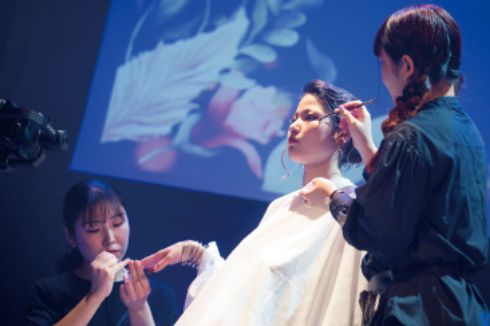 トータルビューティー科の学生がステージ上でモデルにメイクをしている様子