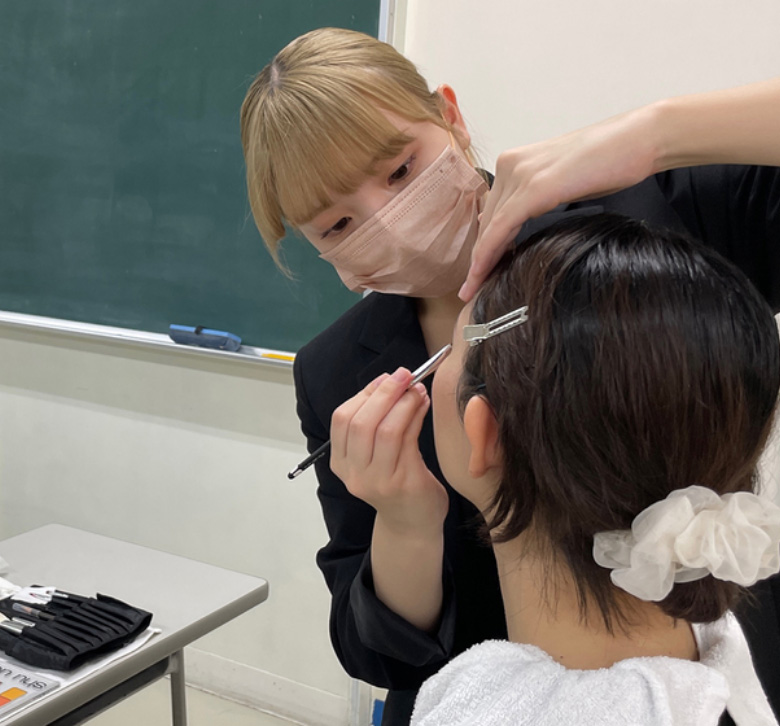 教室で学生がモデルにメイクをしている様子