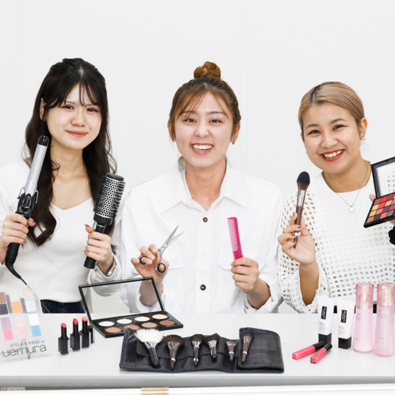 三人の美容学生が笑顔で教材を手に取っている写真