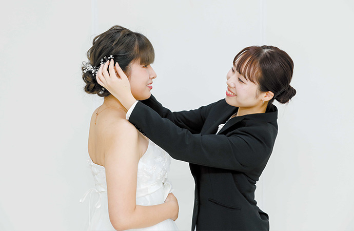 ウェディングドレスを着ているモデルにヘアアレンジをする美容学生