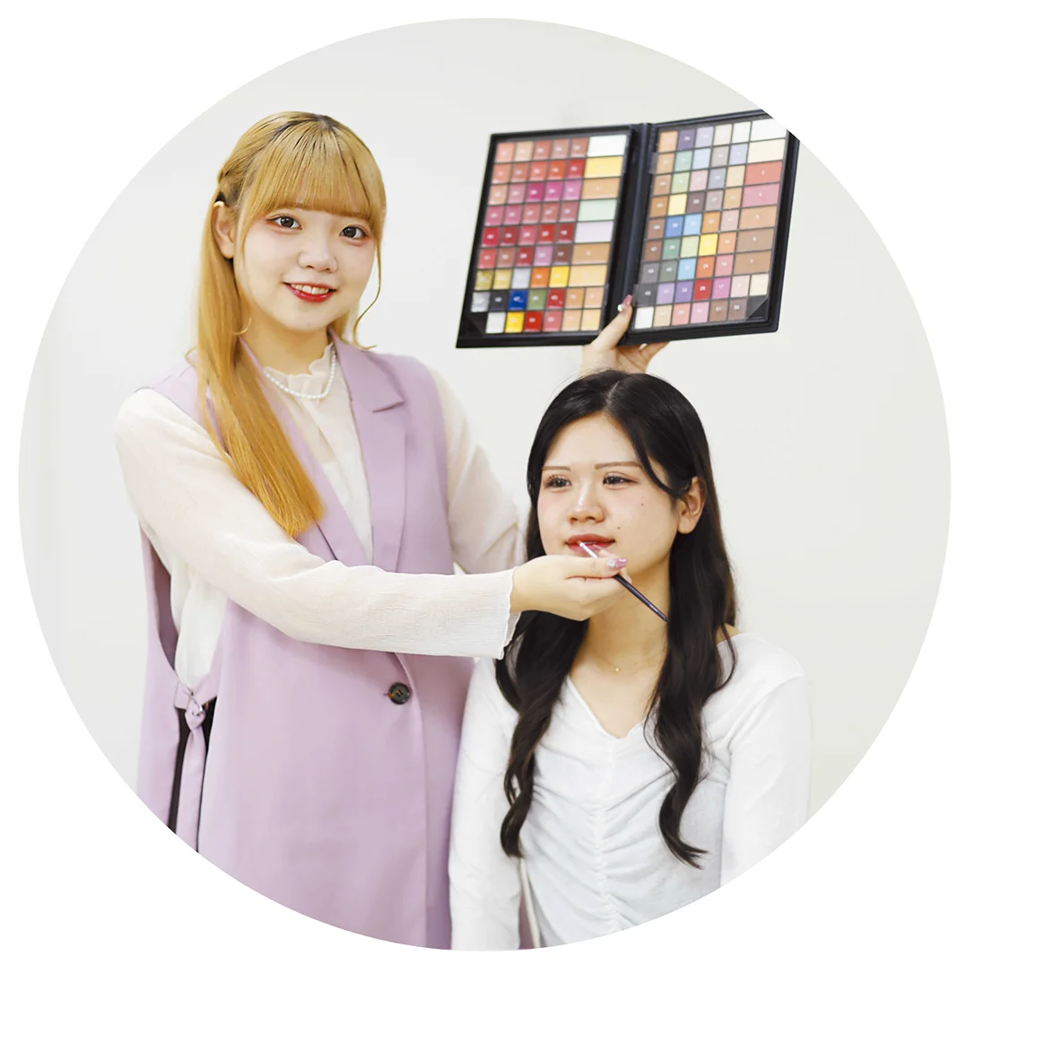 女性の美容学生がモデルにメイクをしている様子