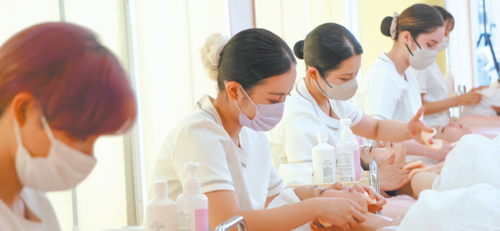 複数の学生がモデルにエステの施術を行なっている写真